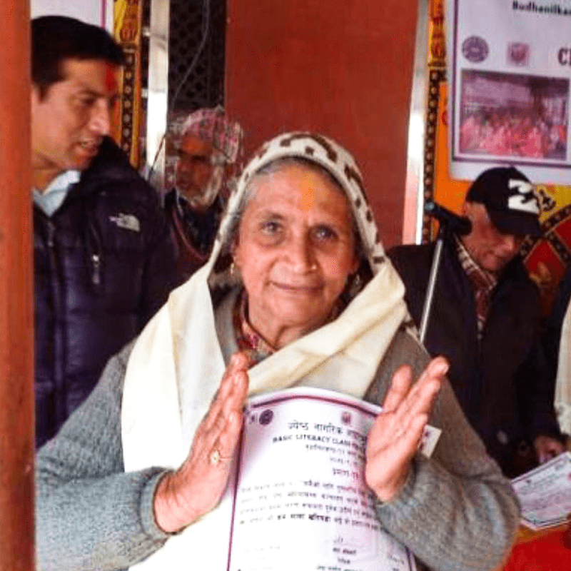 Older woman from Nepal with her literacy diploma, clapping her hands.