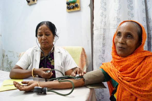 An older women in an orange headscarf has her blood pressure taken by a female doctor