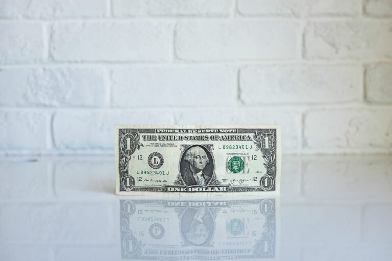A single dollar bill sits on a reflective table.